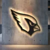 Black metal Arizona Cardinals logo wall art with bright LED backlight on concrete wall.
