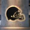 Black metal Cleveland Browns helmet wall art with warm LED backlighting on a concrete wall.