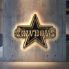 Black metal Dallas Cowboys star logo wall art with bright LED backlight on a concrete wall.