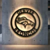 Black metal Denver Broncos logo wall art with warm LED backlight.