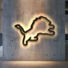 Black metal Detroit Lions logo wall art with bright LED backlighting on a concrete wall.