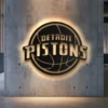 Black metal Detroit Pistons logo wall art with golden details and warm LED backlight.