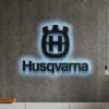 Black Husqvarna metal logo wall art with blue LED backlight on a concrete wall.