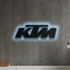 Black metal KTM logo wall art with blue LED backlight.