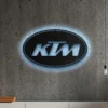 Black metal KTM logo wall art with blue LED backlight on a concrete wall.