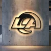 Black metal Los Angeles Rams logo wall art with warm LED glow on concrete wall.