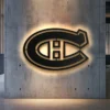 Black metal Montreal Canadiens logo wall art with warm LED backlight on a concrete wall.