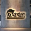 Black metal New England Patriots logo wall art with bright LED backlight on a concrete wall.
