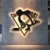 Black metal Pittsburgh Penguins logo wall art with warm LED backlighting on a concrete wall.