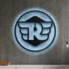 Black metal Royal Enfield logo wall art with blue LED backlight on a concrete wall.