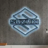 Black metal Suzuki logo wall art with blue LED glow on a concrete wall.