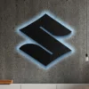 Black metal Suzuki logo wall art with blue LED backlight on concrete wall.