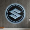 Black metal Suzuki logo wall art with blue LED glow on concrete wall.