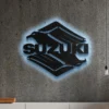 Black metal Suzuki logo wall art with blue LED backlight on concrete wall.
