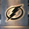 Black metal Tampa Bay Lightning logo wall art with warm LED backlighting on a concrete wall.