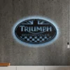 Black metal Triumph Motorcycles logo wall art with blue LED backlighting on a concrete wall.