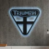 Black metal Triumph logo wall art with blue LED glow on a concrete wall.