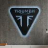 Black metal Triumph logo wall art with blue LED backlight on a concrete wall.