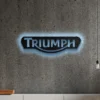 Black metal Triumph logo wall art with blue LED backlight on a concrete wall.