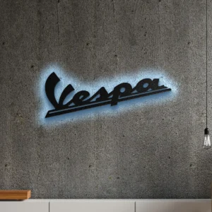 Black metal Vespa logo wall art with blue LED backlighting on a concrete wall.