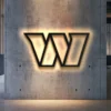 Black metal Washington team logo wall art with warm LED backlight on a concrete wall.